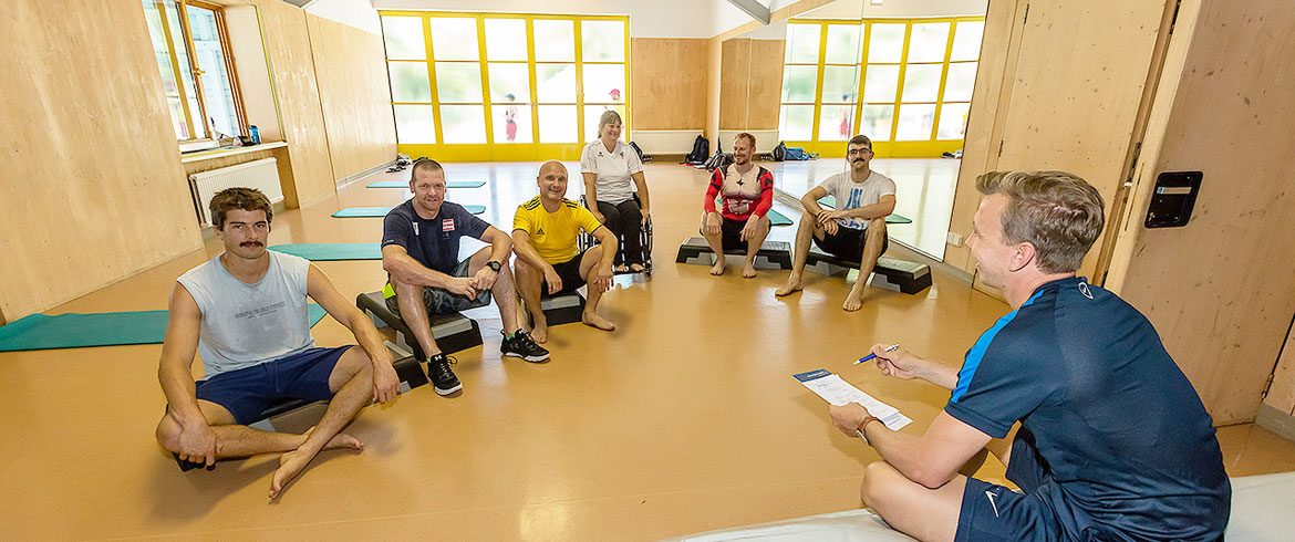 Headerbild der BSPA Wien - Sportgruppe mit Trainer sitzt im Gymnastikraum