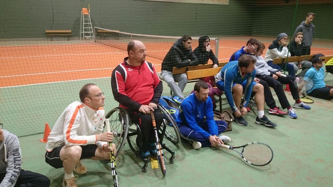 Foto von Tennisspielern am Rand sitzend und dem Vortragenden zuhörend