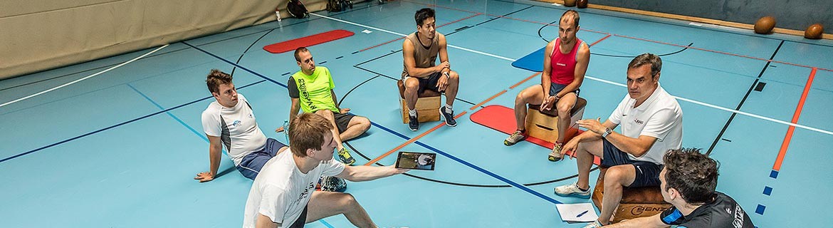 Headerbild der BSPA Wien - Sportgruppe mit Trainer sitzt im Turnsaal