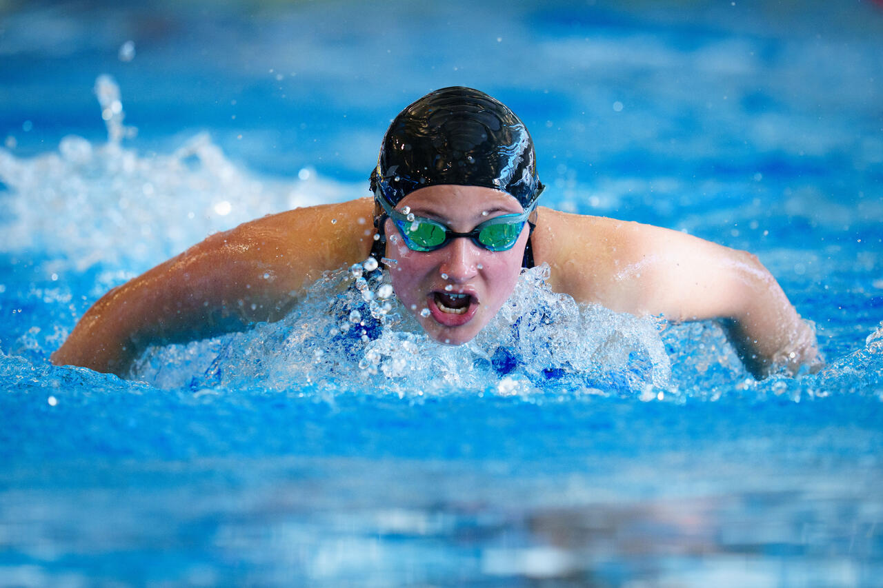 Eine Person mit Badehaube und Schwimmbrille kurz vor dem Eintauchen ins Wasser.