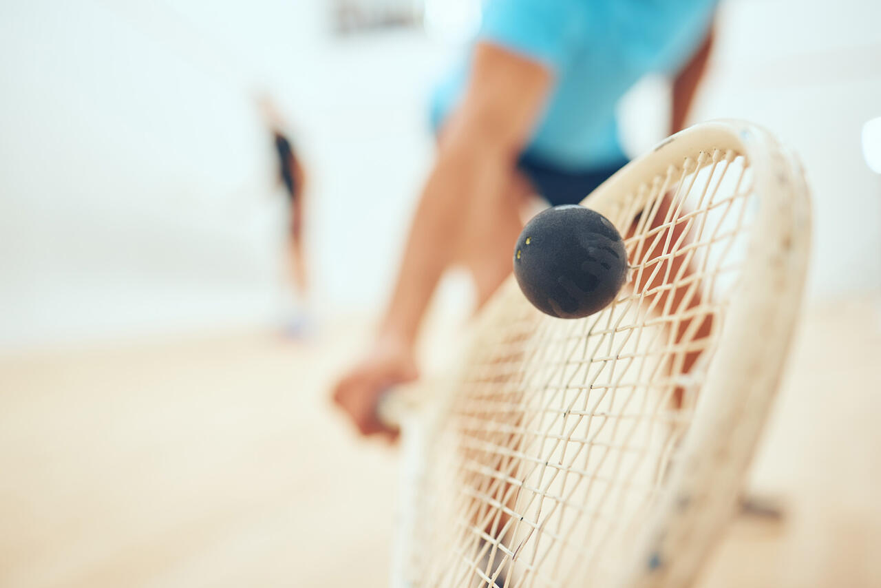 Person hält Schläger und Ball berührt Schlägerbespannung.