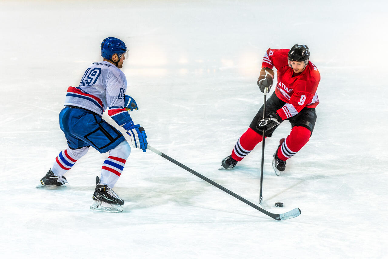 Das Bild zeigt 2 Eiskockeyspieler in Action beim Kampf um den Puck.