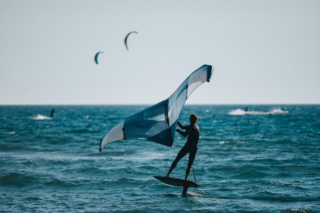 Eine Person am Board im Wasser und einen Wing in den Händen.