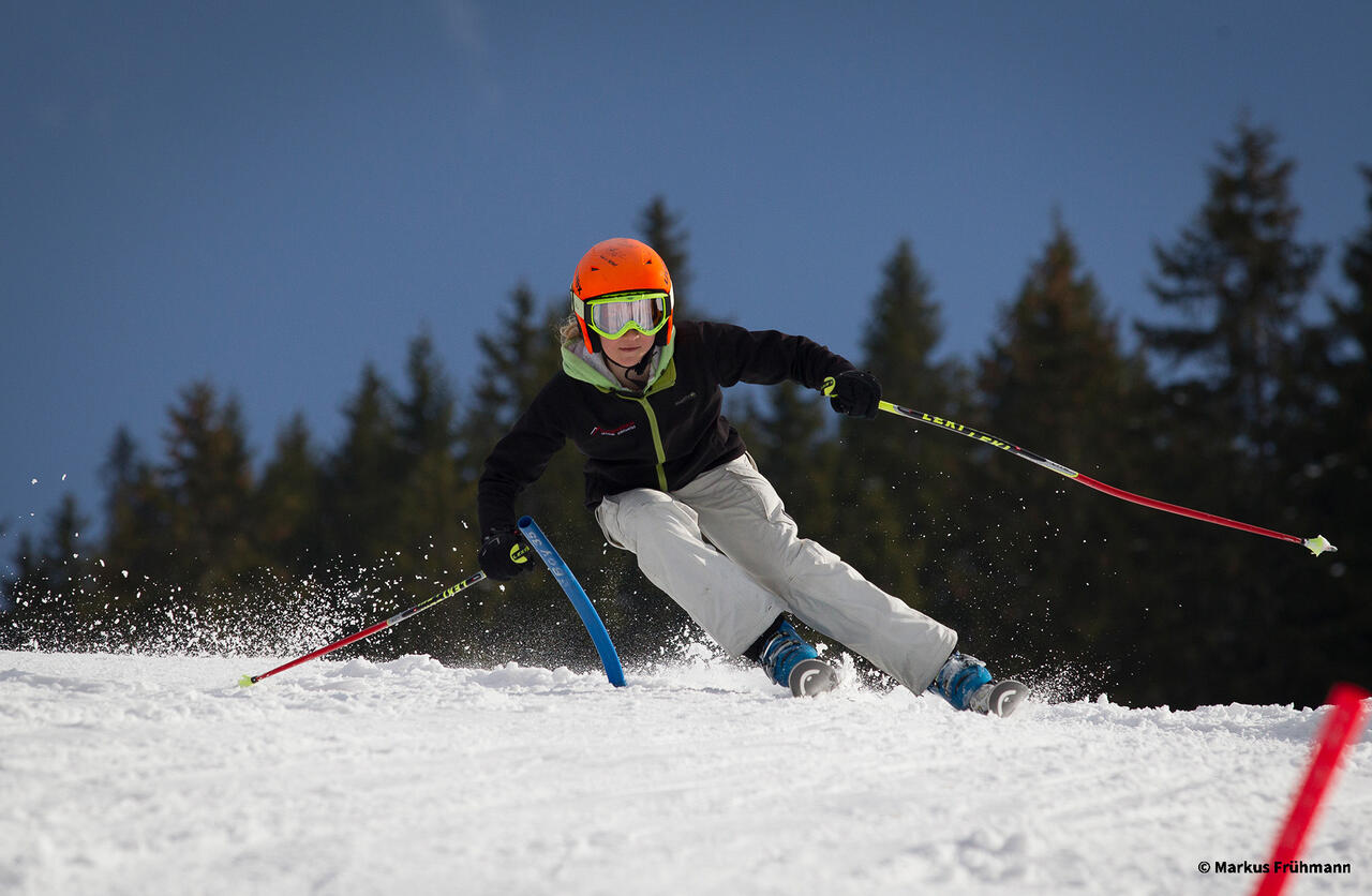 Jugendliche Person auf Ski im Schnee mitten im Schwung.