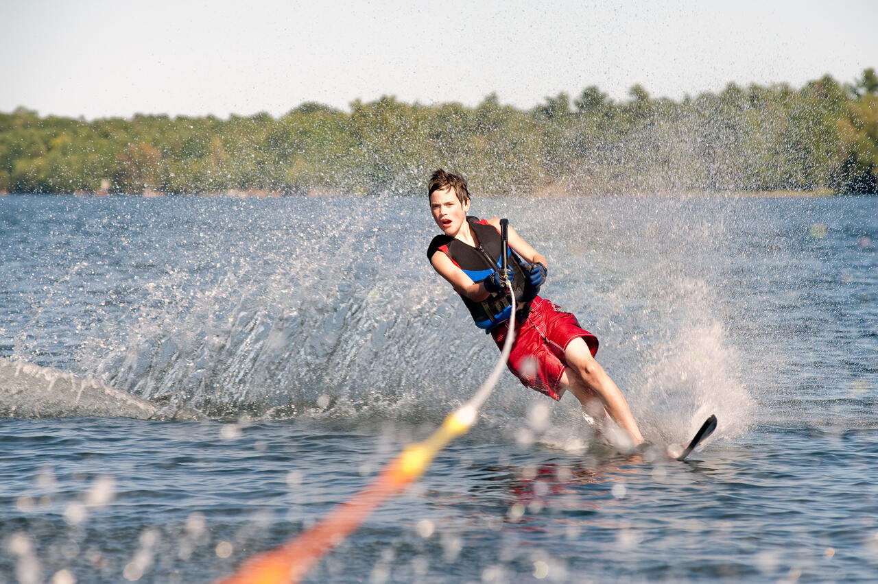 Ein Jugendlicher am Ski im Wasser mit Seil in der Hand.
