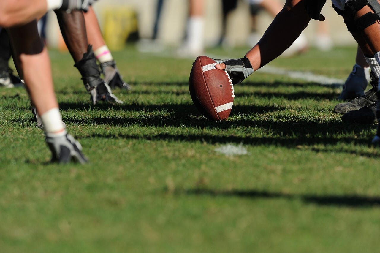 Ausschnitt von mehreren Händen im Gras und eine Person hält Ball im Gras.