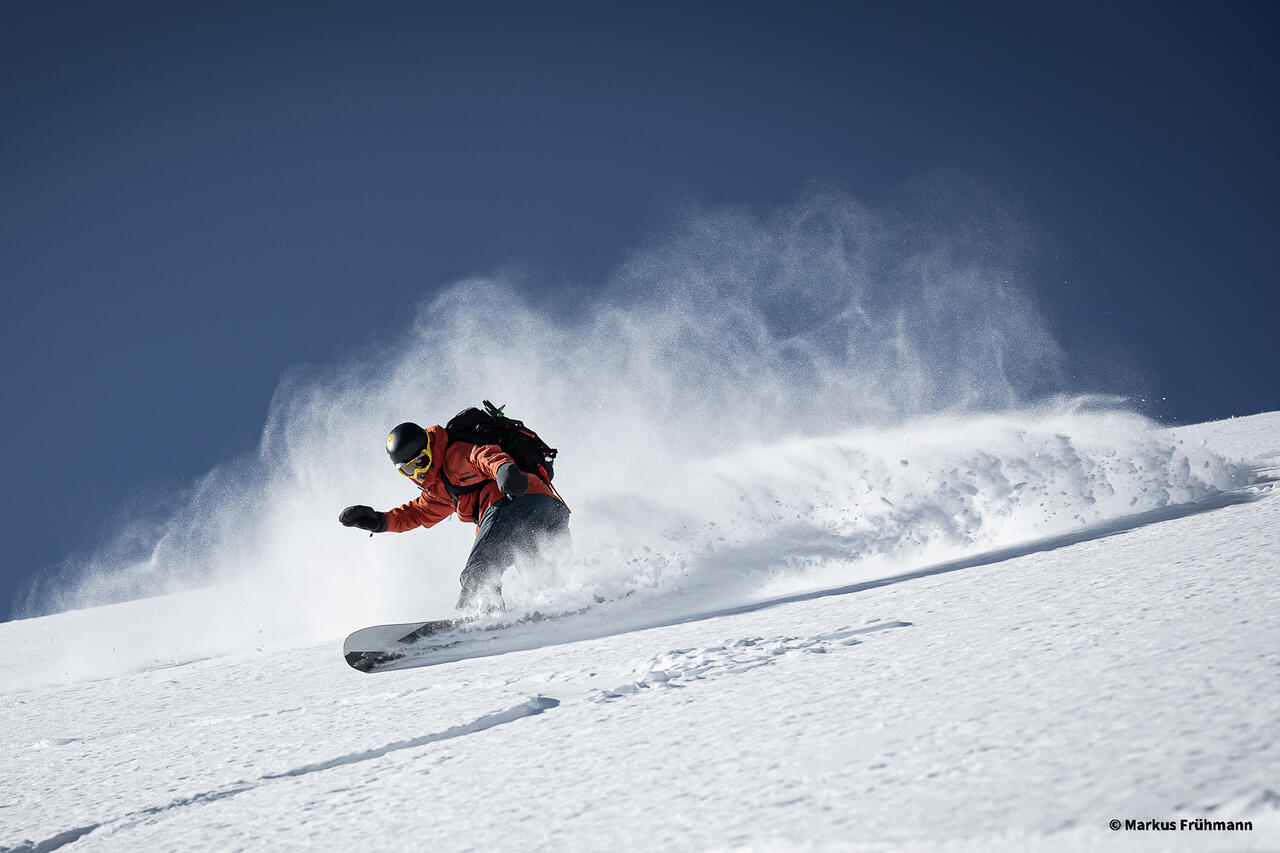 Eine Person beim Snowboarden im staubenden Schnee.