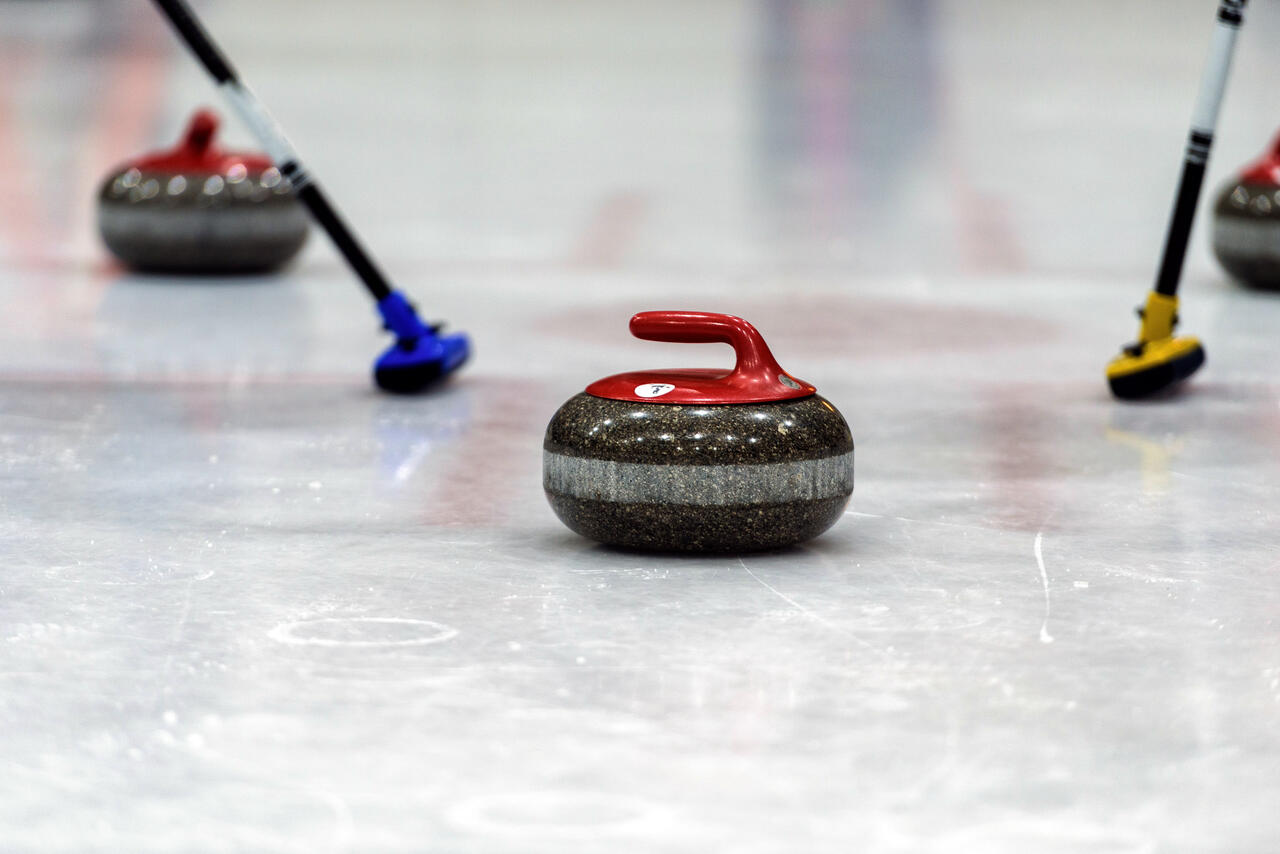 Ausschnitt von drei Curlingsteinen und zwei Besen am Eis.