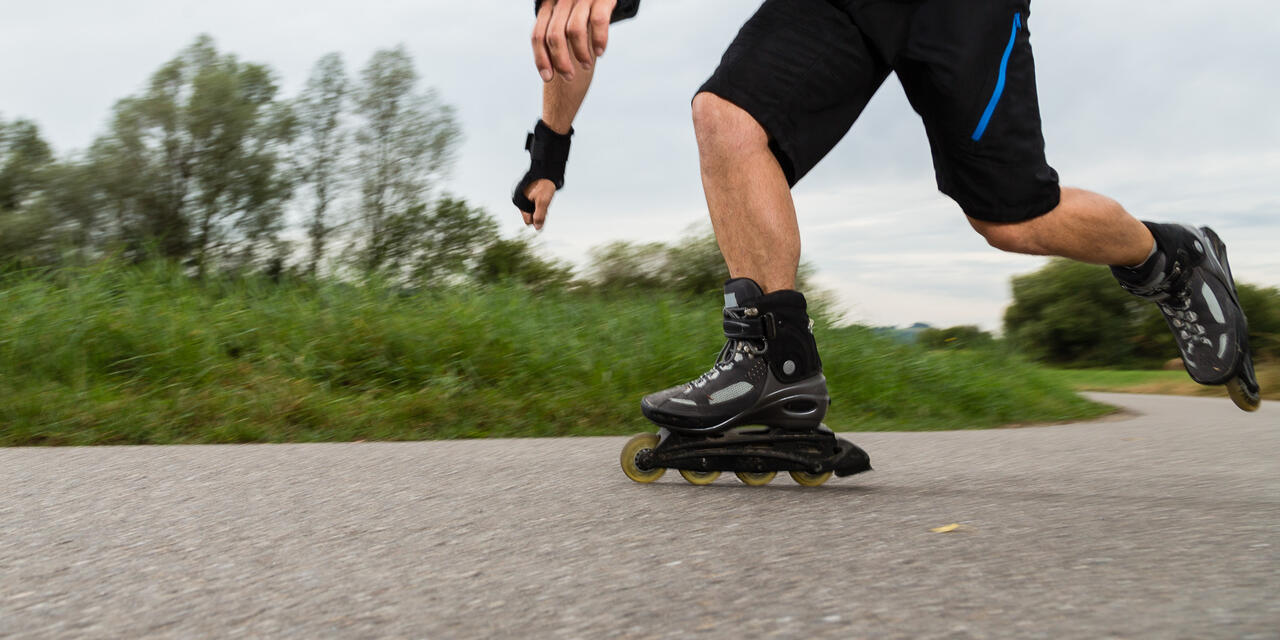 Ein Bein mit Skates am Asfalt, das andere hinten in der Luft.